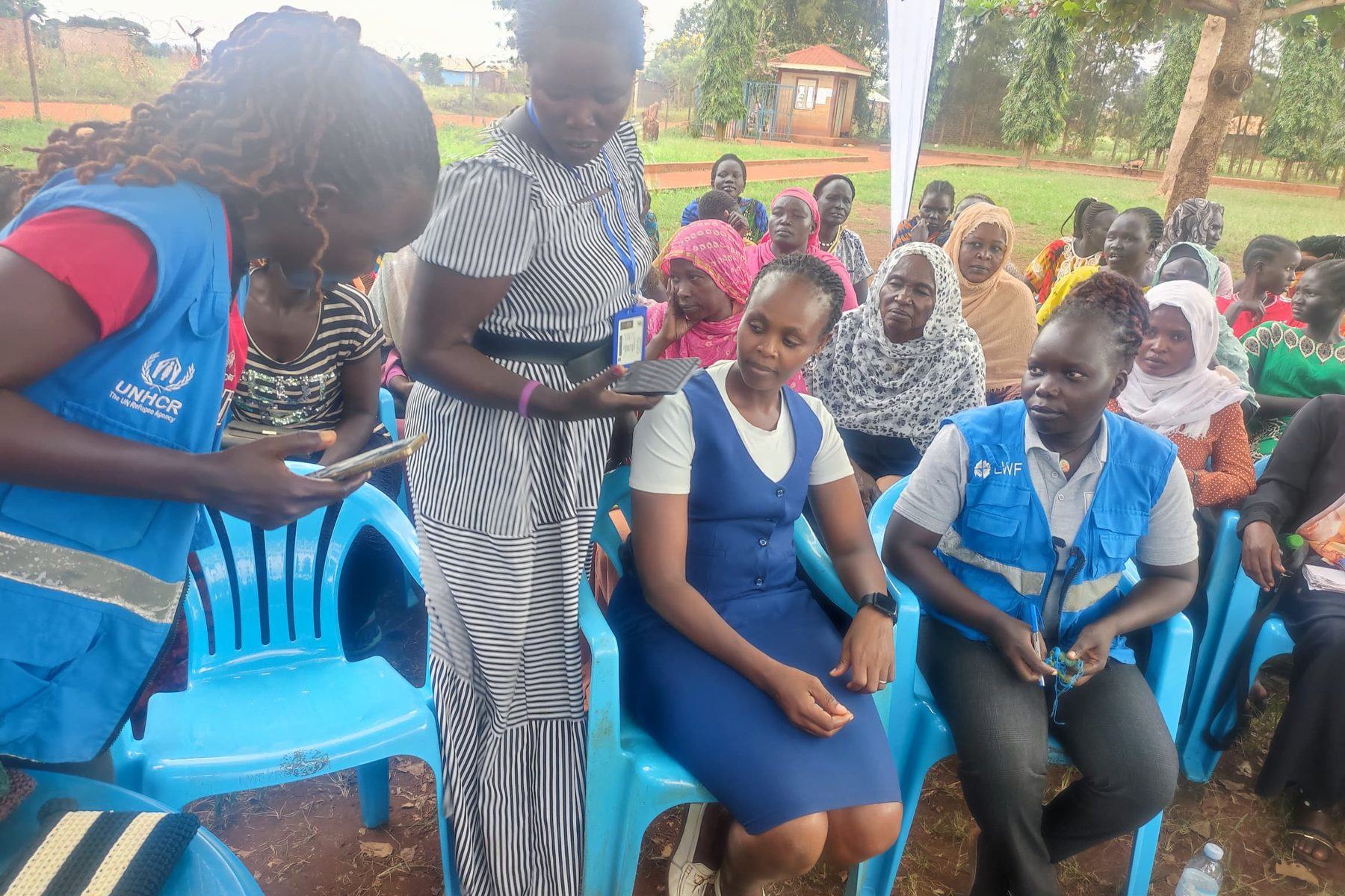 PhiphyMak team members seated with women and children during a community outreach in Kiryandongo Refugee Settlement